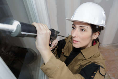 beautiful female construction worker using caulking gun at siteの写真素材