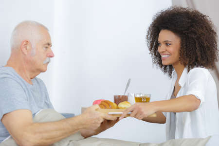 senior man in nursing home having breakfast in bedの写真素材