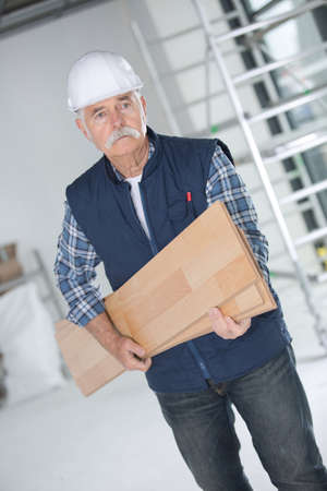 senior carpenter carrying wooden planks at construction siteの写真素材