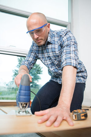 carpenter cutting laminated planks for layered parquet using bandsaw