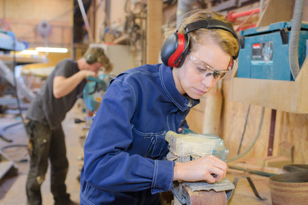 midsection of female carpenter using sander on wood in workshop