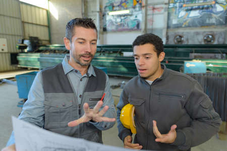 male supervisor with workers discussing over blueprints in industryの写真素材