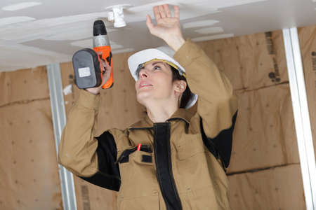 pretty woman with building puncher drilling hole in ceilingの写真素材