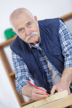 male carpenter marking on wood with pencil in workshopの写真素材