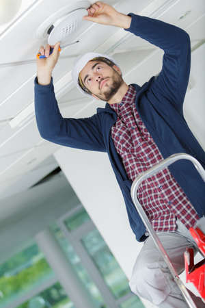 electrician mounts halogen lamp in ceiling light in roomの写真素材