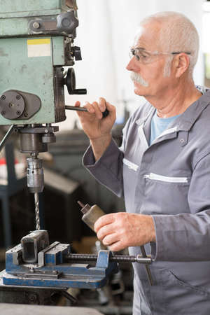 elderly worker watches processing of detail on milling machineの写真素材