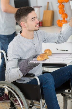 A young man in wheelchair opens the oven to prepare food