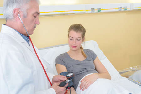 A senior doctor testing blood pressure on a female patientの写真素材