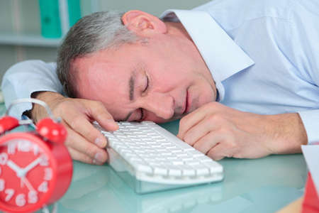 man sleeping on his desk in bright modern officeの写真素材