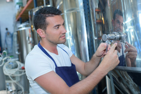manufacturer filling beer into glass from storage tank at brewery