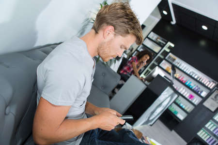 male customer with phone waiting at hair salonの写真素材