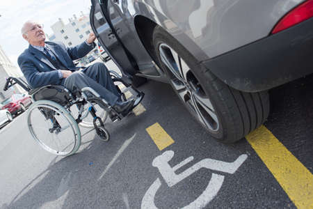 senior handicapped driver waiting for assistant to go in carの写真素材