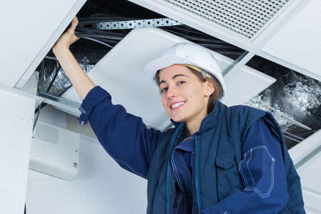 female electrician installing electric device in ceilingの写真素材