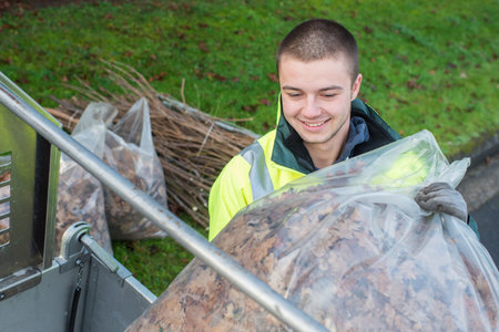 young worker loading bag of dead leaves into vehicle
