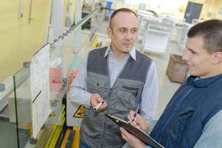 manager noting on clipboard and worker taping box in warehouseの写真素材