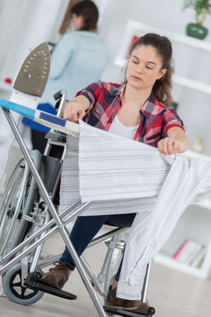 disabled young pretty woman ironing in her living roomの写真素材