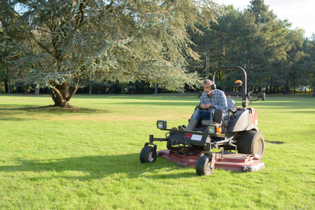 gardener cutting grass of a garden on a lawn mower