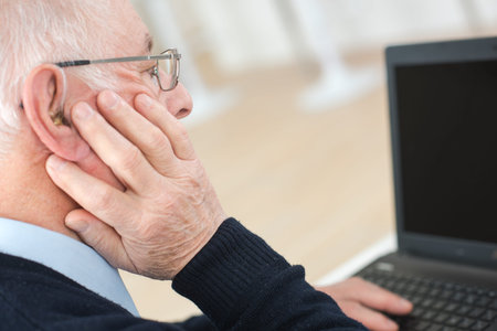 senior man suffering from deafness with computer