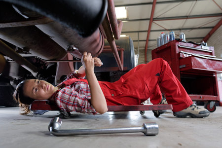 portrait of female auto mechanic working underneath car