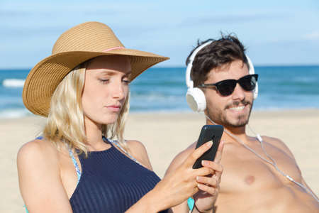 couple using their phones on the beachの写真素材