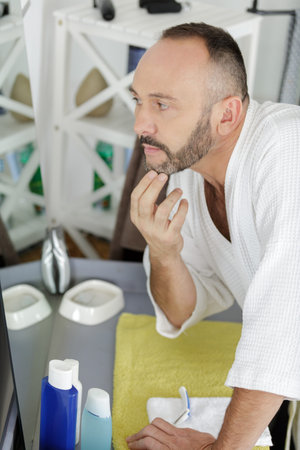 man putting on face cream looking in the mirror