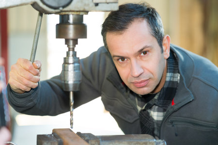 portrait of middle-aged male worker by hydraulic bench drill