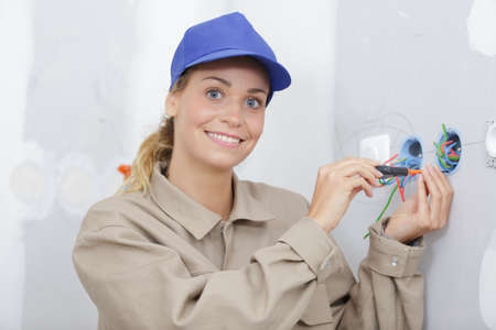 young female electrician wiring electrical socket on wallの写真素材