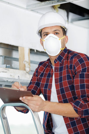 adult male builder renovating with drill in mask and helmet