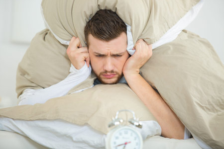 man burying head under pillow to lesson alarm clock noise