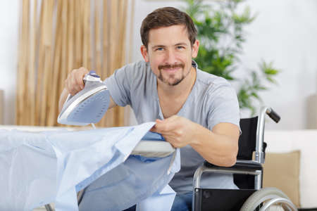happy disabled man ironing shirts at homeの写真素材
