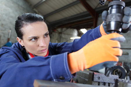 female apprentice using drill in factory