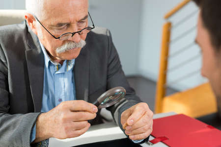 senior man looking through a magnifying glass on a itemの写真素材