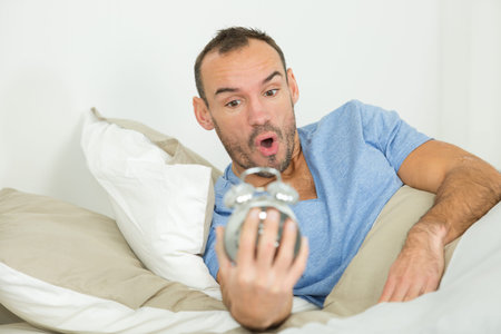 man in bed looking in shock at the alarm clock