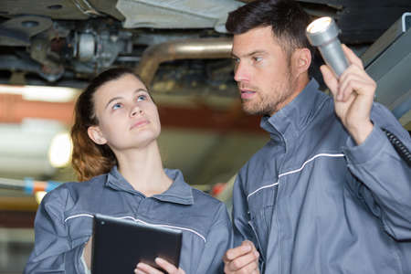 mechanics working underneath a lifted car holding torch and tabletの写真素材