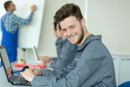 young man in overalls using laptop during training courseの写真素材