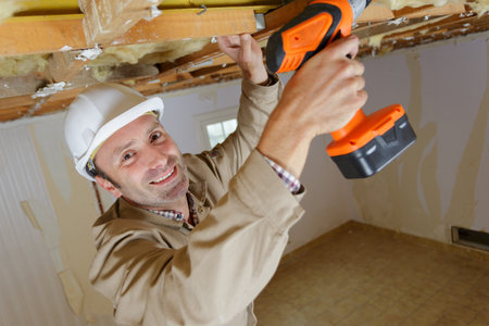 portrait of male builder using cordless drill on wooden beam