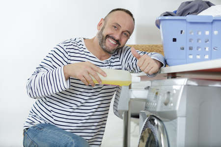 man pouring detergent into washing machine drawerの写真素材