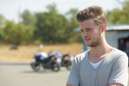 young man posing with motorbike in the background