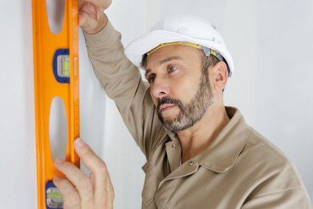engineer in helmet is measuring wall with level