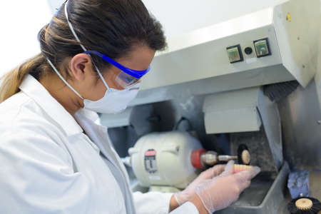 female worker shaping prosthetic teeth on grinding machineの写真素材