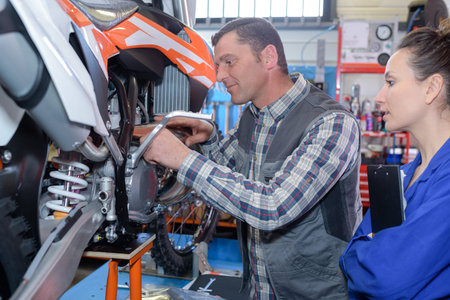 female and male worker repairing motorcycle in workshop