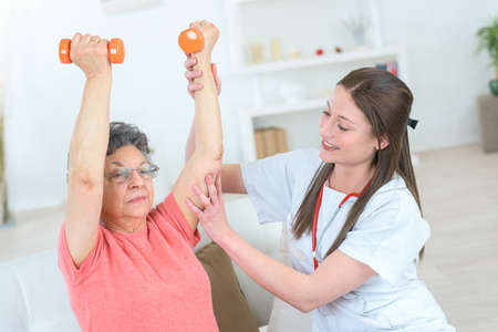 nurse assisting elderly woman on her weights workoutの写真素材