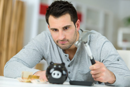 young man breaking piggy money bank with hammer