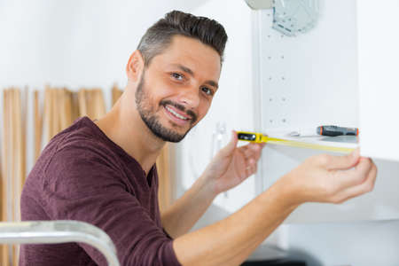 man smiling while measuring the cupboardの写真素材
