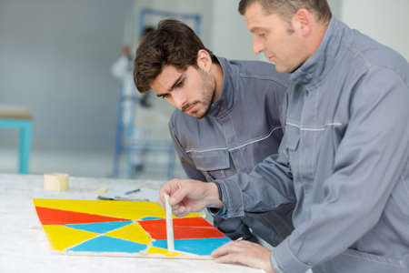 painter and apprentice practicing pattern on benchの写真素材