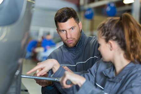 mechanic advising female apprentice tightening wheel nutsの写真素材