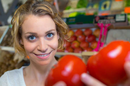 Glad young female customer choosing fresh ripe tomatoes on marketの写真素材