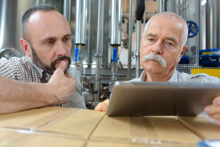 close view of two male brewery workers looking at tabletの写真素材