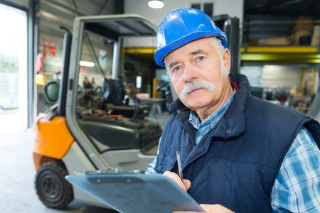 senior worker with a clipboard working on a forklift