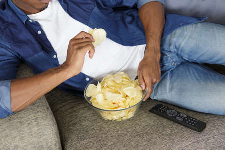 man watching tv and eating chipsの写真素材